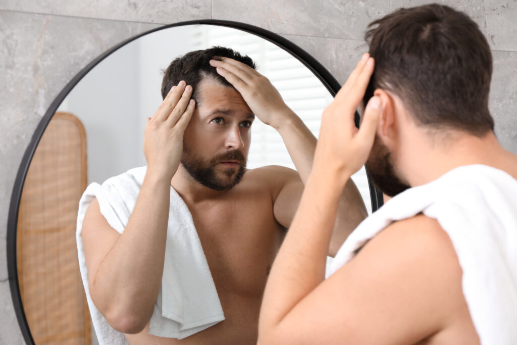 A man checking his hairline in a bathroom mirror