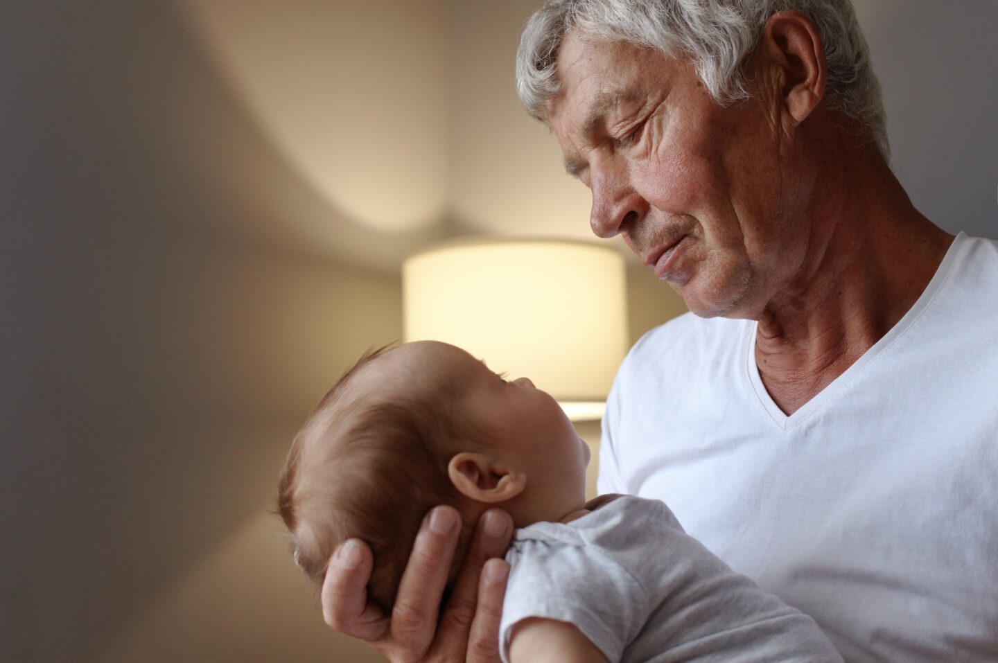 Grandfather tenderly holding his newborn grandchild at home, a reminder of why whooping cough vaccination protects newborns